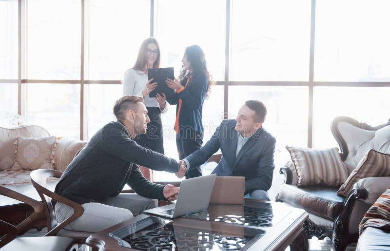 Welcome on board Two handsome men shaking hands with smile at office with their coworkers. Young team of coworkers