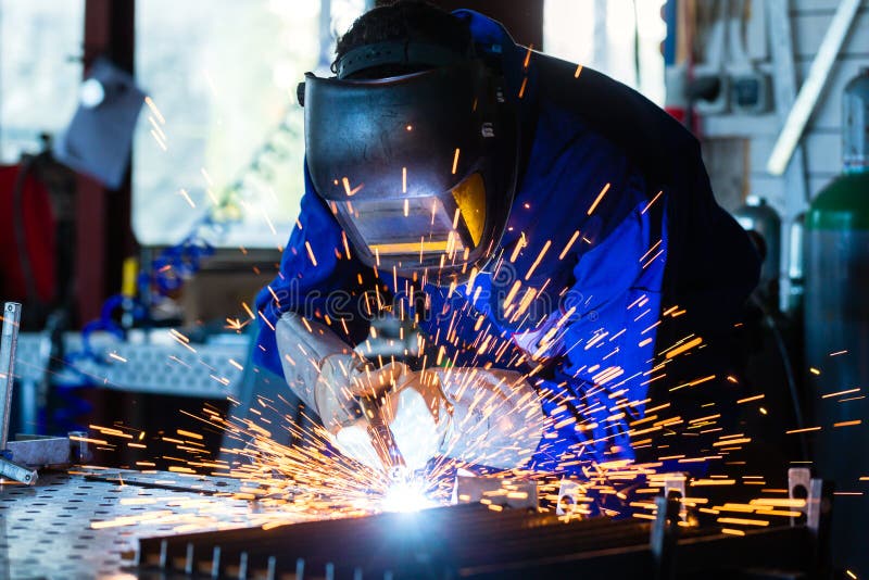 Welder welding metal in workshop with sparks