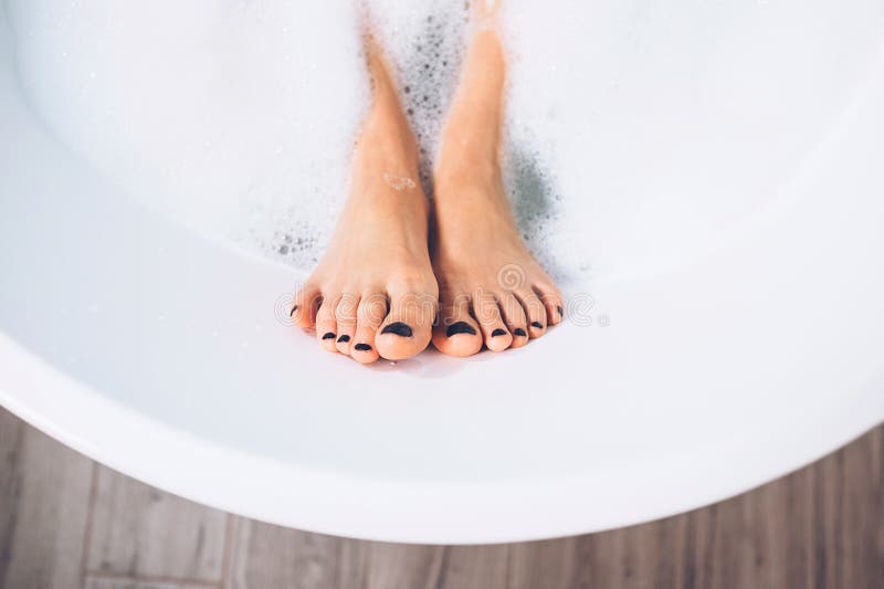 Well groomed woman`s legs in bath foam close up image