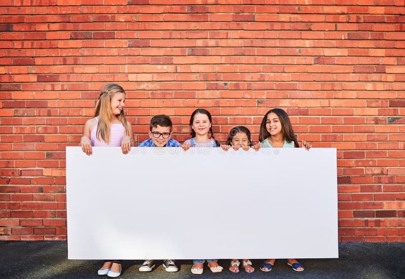 Well keep an eye on this space for you. Portrait of a group of young children holding a blank sign against a brick wall. royalty free stock photography