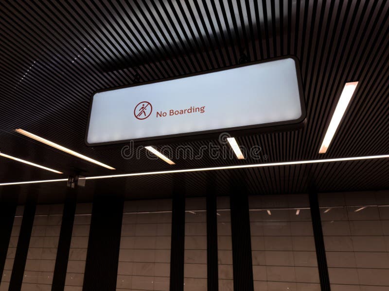 Well lit modern metro station interior with large illuminated No Boarding sign hanging from the ceiling, emphasizing rules and stock images