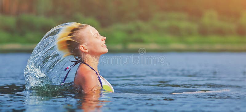 Active young blonde woman waving hair splashing water in river. Beautiful healthy lady relax and laughing, raising head out of the water. Vacation in paradise enjoying swimming. Motion freeze. Active young blonde woman waving hair splashing water in river. Beautiful healthy lady relax and laughing, raising head out of the water. Vacation in paradise enjoying swimming. Motion freeze