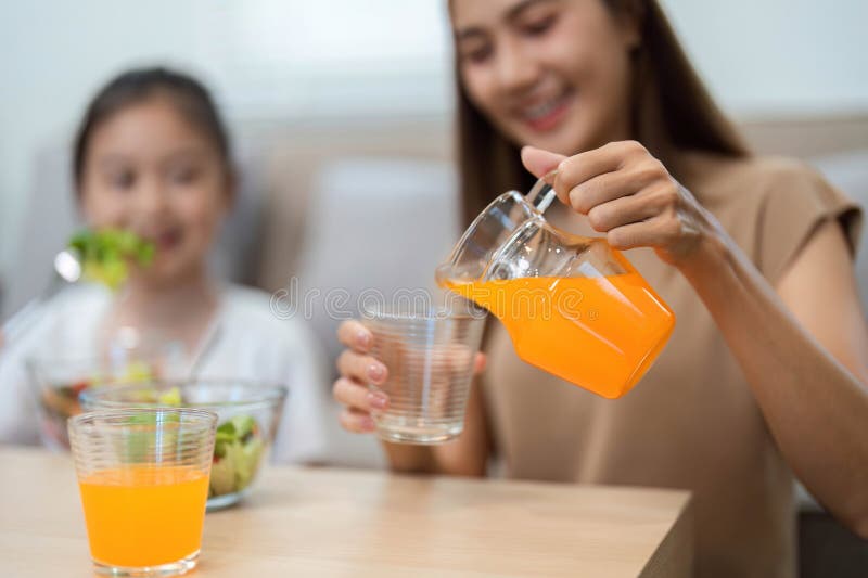 Wellness through healthy drinking: Mother pouring orange drink stock images
