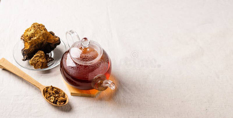 Wellness tea from chaga tree mushroom in a glass teapot and glass. Organic drink antioxidant gray natural background.
