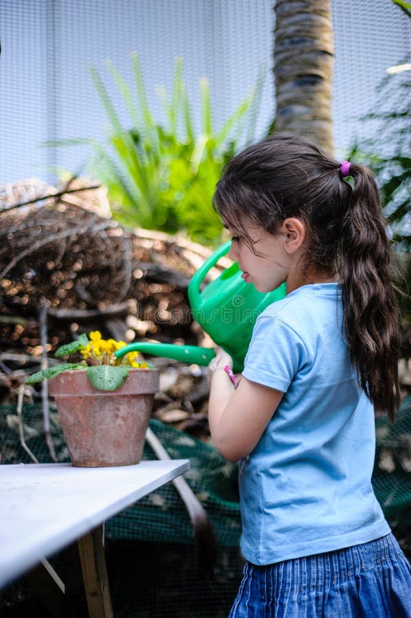 Wenig Mädchenkinderbewässerungsblumentopf im Garten mit der Gießkanne