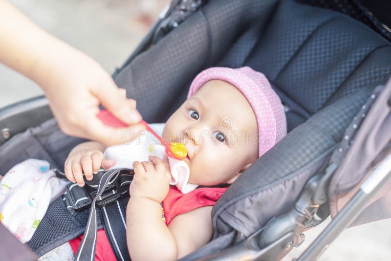 Wenig nettes Baby sitzt auf einem Stuhl und dem Essen mit Löffel Das Fütterungsbaby der Mutter, das heraus ihre Hand mit einem Lö stockbild Wenig nettes Baby sitzt auf einem Stuhl und dem Essen mit Löffel Das Fütterungsbaby der Mutter, das heraus ihre Hand mit einem Lö stockbild