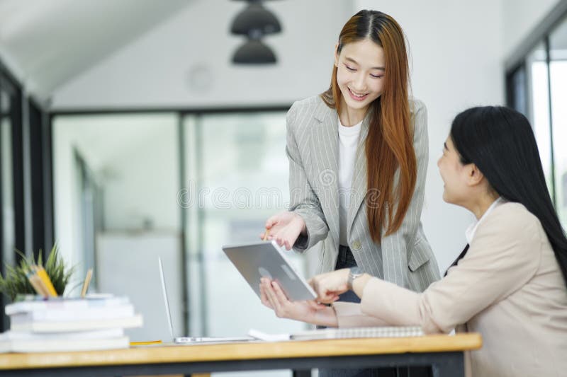 Office woman is standing and teaching a new employee. It describes the work format displayed on the tablet screen. Office woman is standing and teaching a new employee. It describes the work format displayed on the tablet screen.
