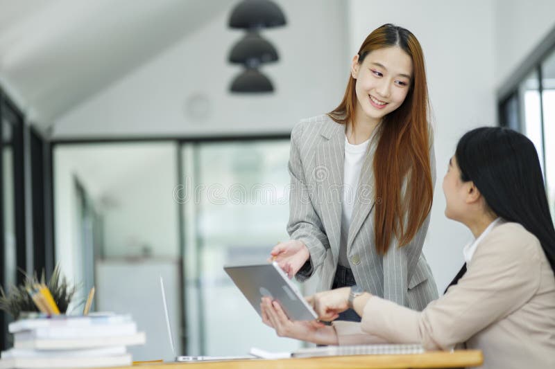 Office woman is standing and teaching a new employee. It describes the work format displayed on the tablet screen. Office woman is standing and teaching a new employee. It describes the work format displayed on the tablet screen.