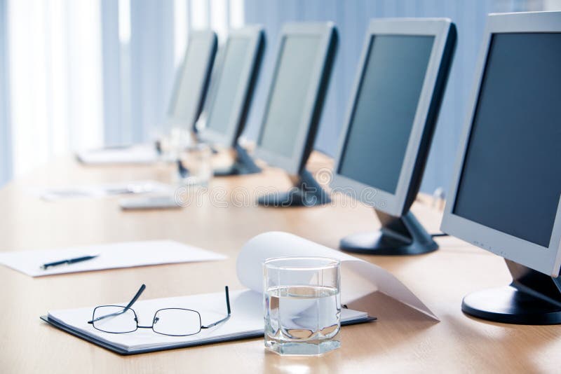 Close-up of workplace with notepad, glass of water, eyeglasses and monitors on it. Close-up of workplace with notepad, glass of water, eyeglasses and monitors on it