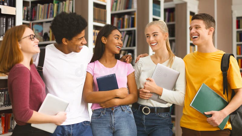 Wesoli studenci międzynarodowi rozmawiający w bibliotece uniwersyteckiej zdjęcia royalty free