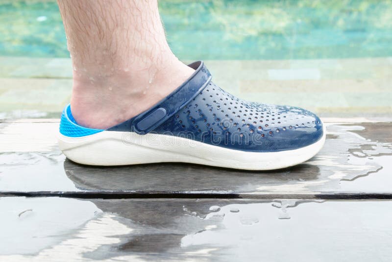 Wet male hairy leg in comfortable rubber summer shoes on the wooden deck by the pool. Wet male hairy leg in comfortable rubber summer shoes on the wooden deck by the pool.