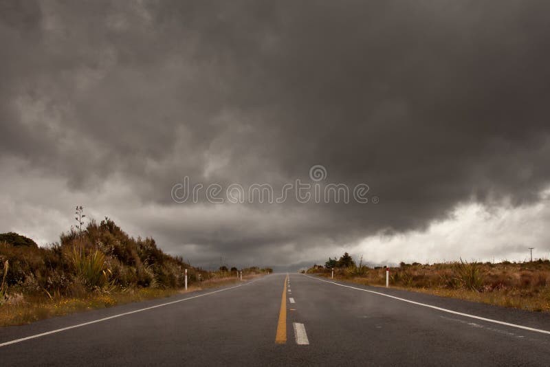 Wet road leading into a storm cloudy sky