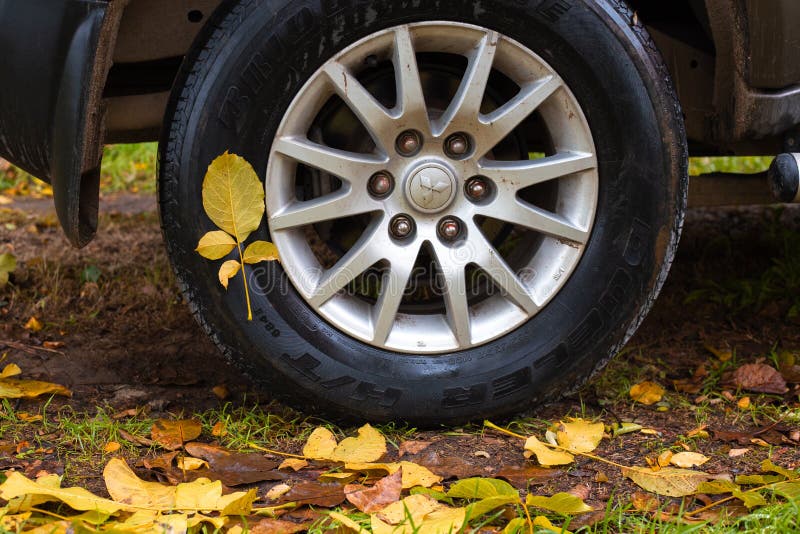 Wet yellow leaves stuck to the tire of a Mitsubishi car on an autumn day. Change of season, rearrange tires for winter