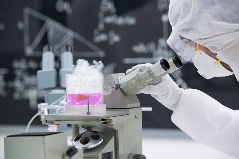 Close-up of scientist analyzing under microscope in a chemistry lab around pink coloured liquid and gas with a blackboard on the background;. Close-up of scientist analyzing under microscope in a chemistry lab around pink coloured liquid and gas with a blackboard on the background;
