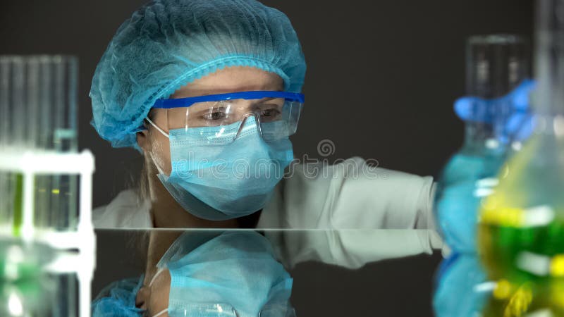 Wetenschapper in het beschermende eenvormige bekijken blauwe vloeistof in fles, wateranalyse stock afbeelding Wetenschapper in het beschermende eenvormige bekijken blauwe vloeistof in fles, wateranalyse stock afbeelding