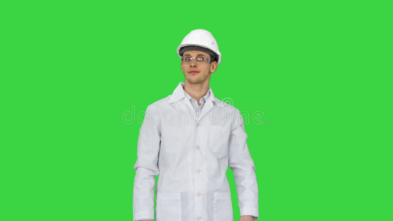 Wetenschapper ingenieur in white robe safety helm en bril die grappige bewegingen maakt met zijn ogen aan het eind op een groene