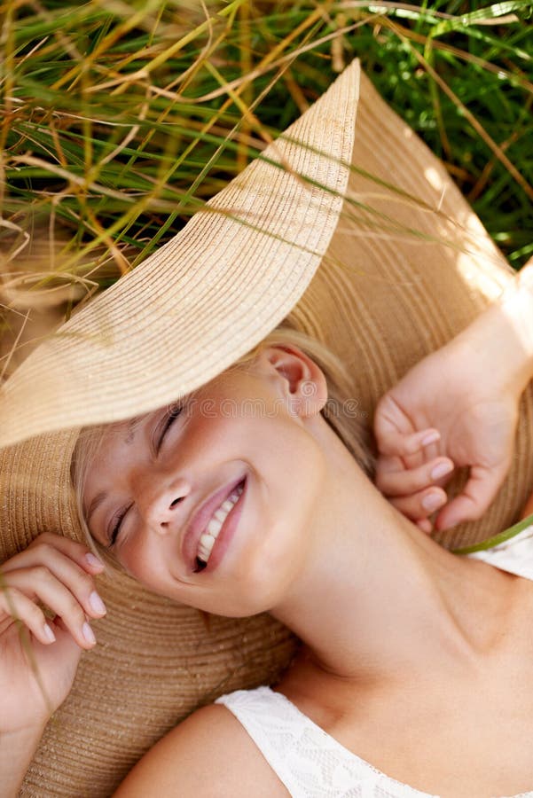 This is what summer was made for. a beautiful young woman in a sunhat lying in tall grass.