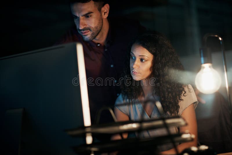 Whatever it takes, whatever the hour. two colleagues using a computer together during a late night at work. royalty free stock photography