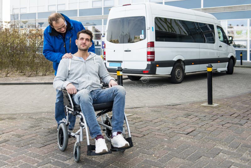 Disabled men in a wheel chair and his male nurse being dropped off at a hospital by a wheel chair taxi