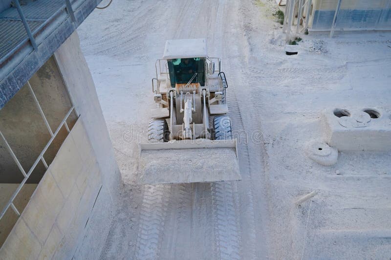 Wheel loader transports calx products in bucket at silica factory in evening. Transportation about large manufacturing industrial complex. Wheel loader transports calx products in bucket at silica factory in evening. Transportation about large manufacturing industrial complex