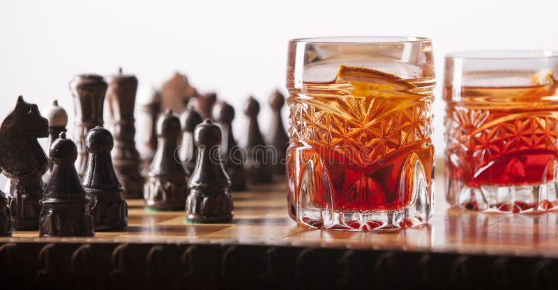 Focused man sipping alcoholic beverage while thinking about next chess move.  Stock Photo by DC_Studio