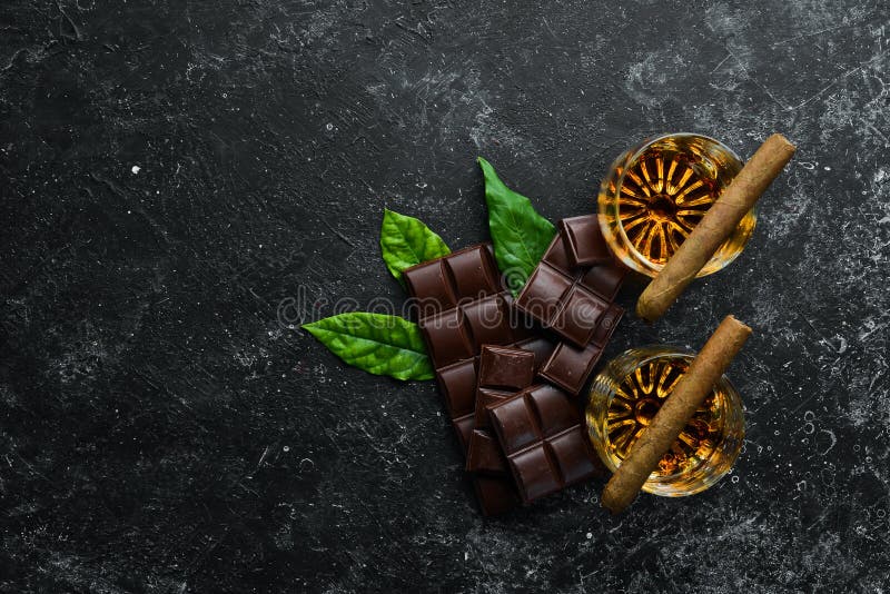Whiskey, chocolate and cigars on a black stone table. Top view. Free space for your text. Whiskey, chocolate and cigars on a black stone table. Top view. Free space for your text