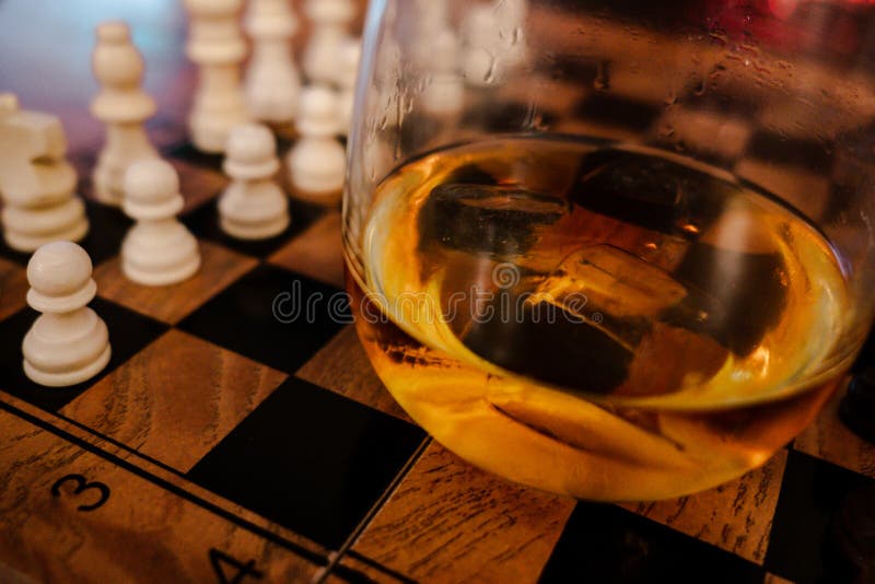 Focused man sipping alcoholic beverage while thinking about next chess move.  Stock Photo by DC_Studio