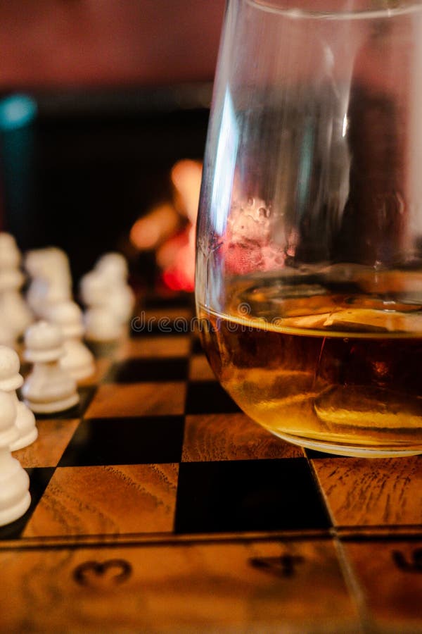 Focused man sipping alcoholic beverage while thinking about next chess move.  Stock Photo by DC_Studio