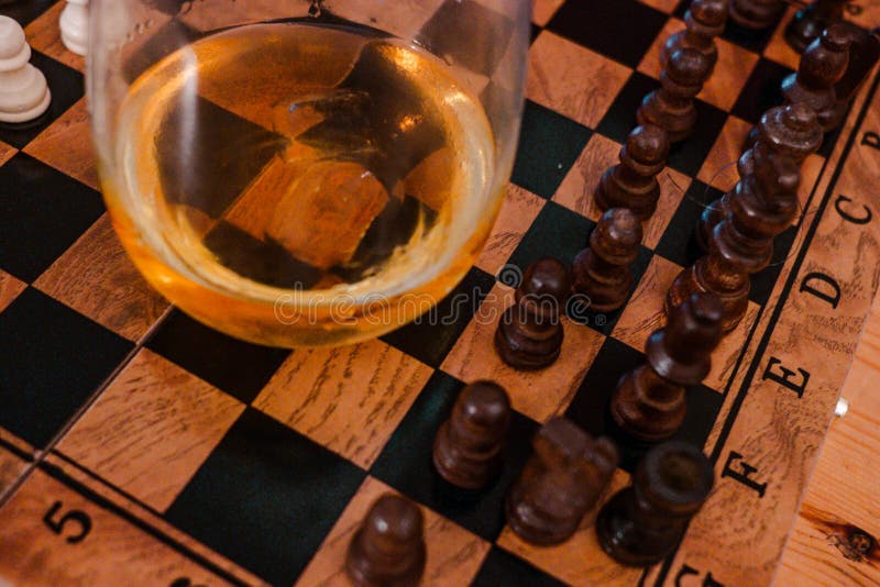 Focused man sipping alcoholic beverage while thinking about next chess move.  Stock Photo by DC_Studio