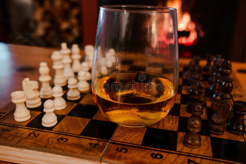 Focused man sipping alcoholic beverage while thinking about next chess move.  Stock Photo by DC_Studio