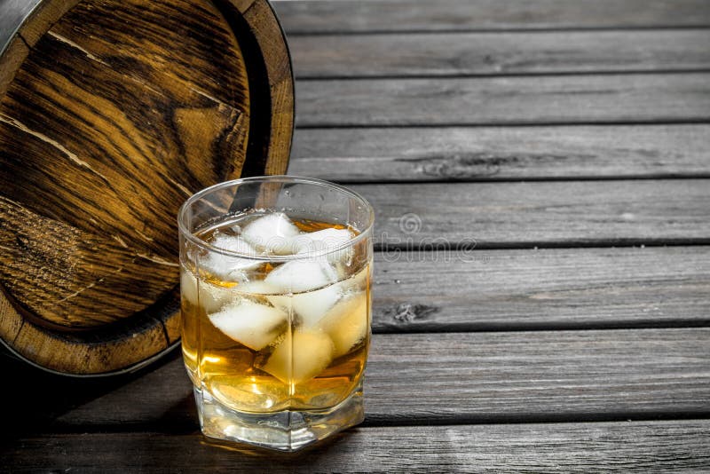 Whiskey in a glass with ice cubes and a barrel