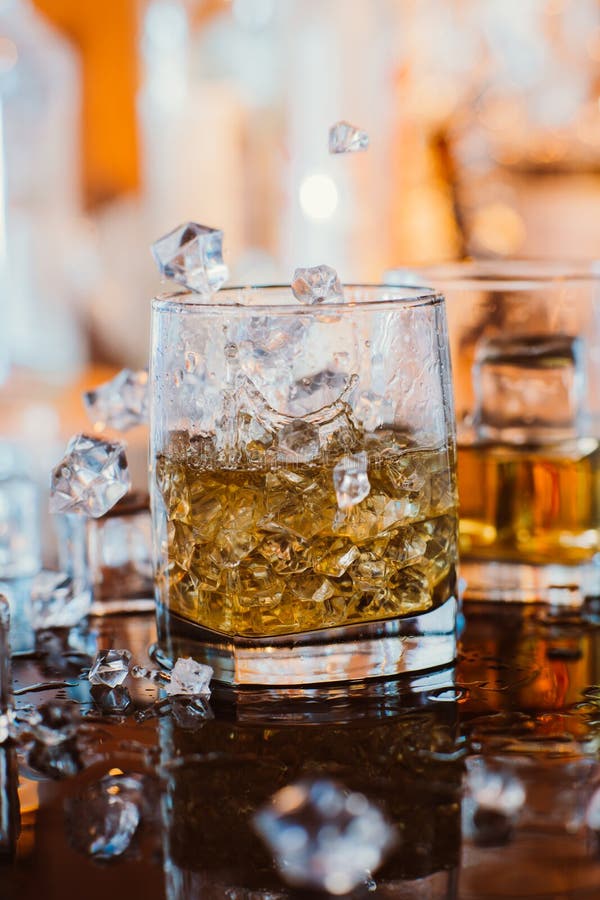 Whiskey glass with ice and warm light on black table with reflection, warm atmosphere