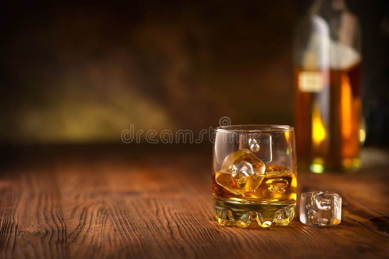 Whisky on the rocks. Glass of whiskey with ice cubes over wooden background