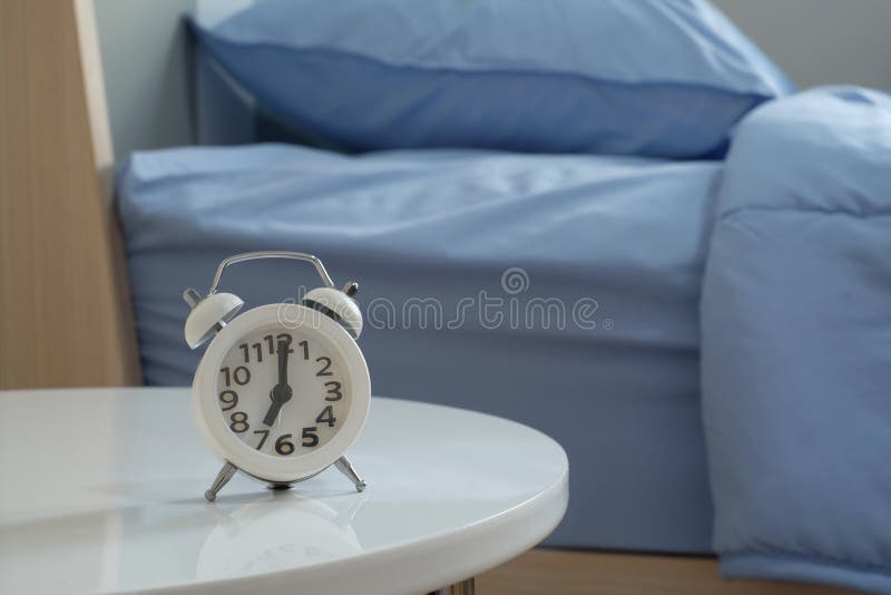 White Alarm Clock at 7 am on the White Table in Bedroom Stock Image