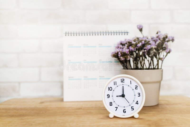 White analog clock with blurred white calendar and purple flower in ceramic vase on wooden desk stock photos White analog clock with blurred white calendar and purple flower in ceramic vase on wooden desk stock photos