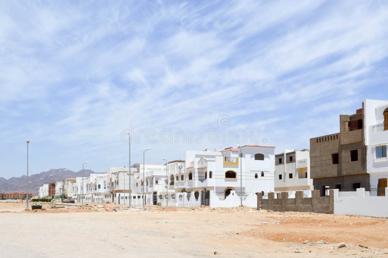 Arabian rectangular and square downtowns, houses in the desert with windows against the background of yellow sand and beautiful bl royalty free stock photo