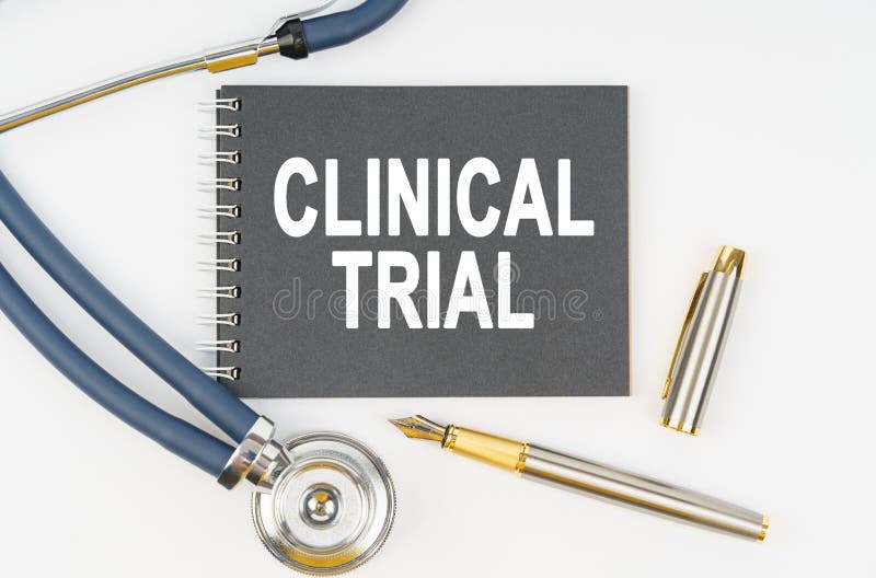 On a white background lie a stethoscope, a pen and a notebook with the inscription - CLINICAL TRIAL