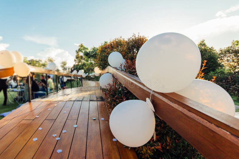 White balloons hanging around a wooden bridge the floor is sprinkled with roses. People come to congratulate the couple