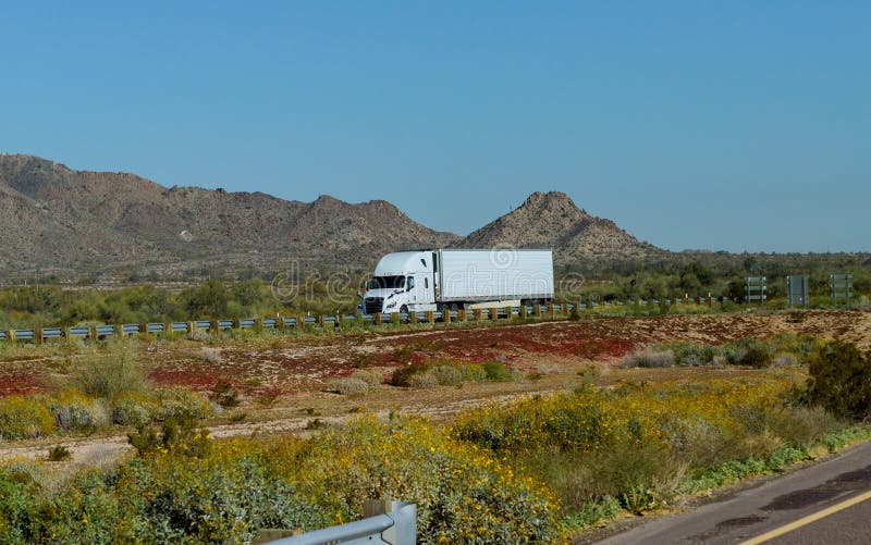 White big rig American long haul semi truck with moving on wide divided turning highway with mountain