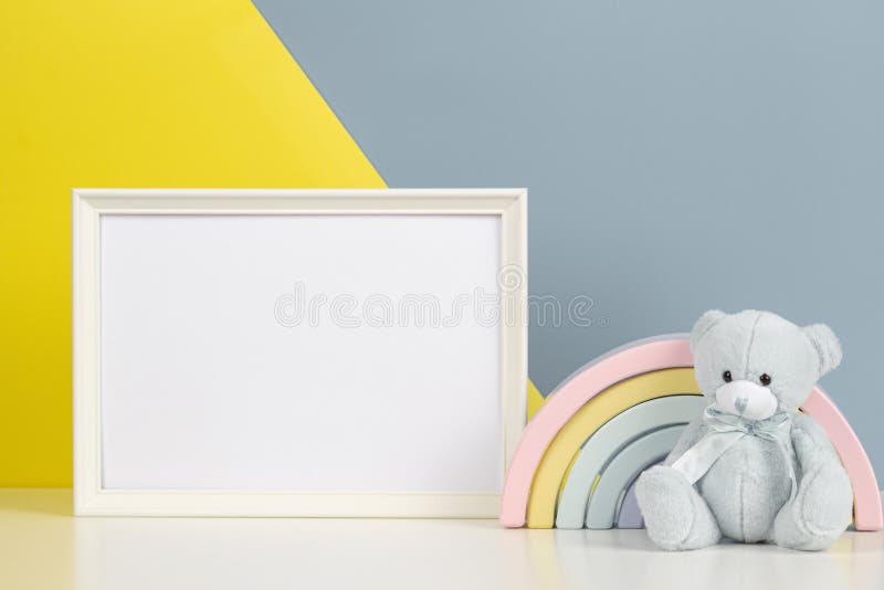 White blank frame with teddy bear and kid toy rainbow on white desk and yellow and gray background