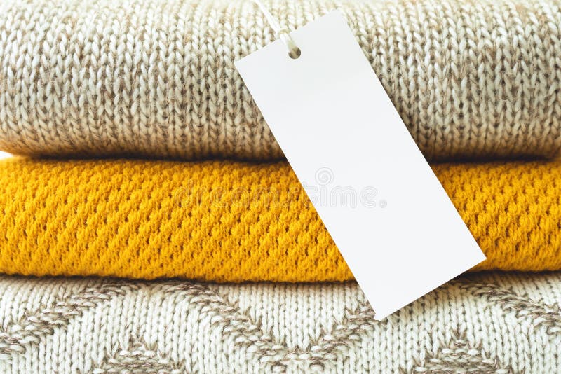 White Blank Rectangular Clothing Tag on Stack of Knitted Clothes