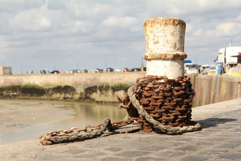 A white bollard with a rusty chain closeup at the harbour in normandy royalty free stock photography A white bollard with a rusty chain closeup at the harbour in normandy royalty free stock photography