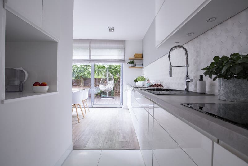 White cabinets in bright modern kitchen interior of house with terrace. Real photo