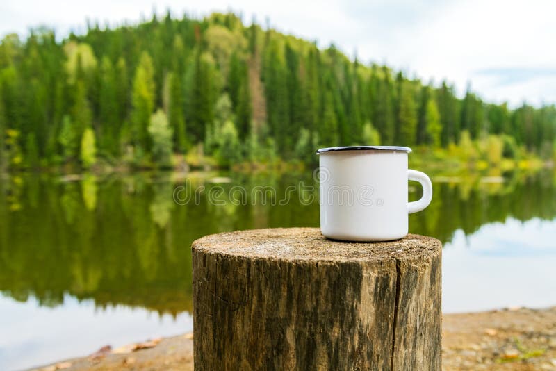 White campfire mug mockup with river bank view. White campfire enamel coffee mug mockup witn the tree stump and river bank view. Empty mug mock up for design
