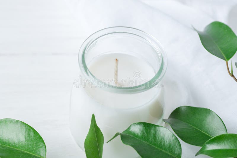 White Candle in Glass Jar Fresh Tree Branches with Tender Green Leaves on Wood and Cotton Linen Fabric Background. Spa Wellness Body Care Meditation Purity Concept. Minimalist Style. Copy Space