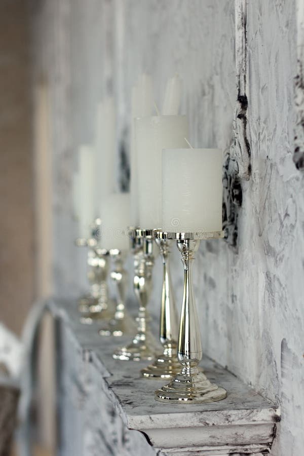 White Candles in Elegant Candlesticks Stand on a Fireplace Stock Photo