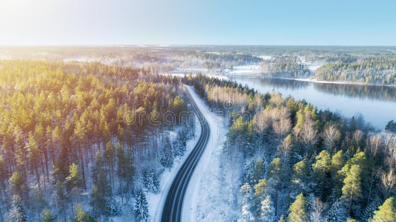 White car drives empty road running along the beautiful blue lake in the cold Finnish winter