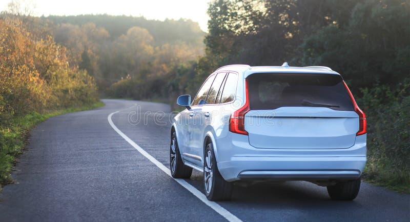 White car driving down a winding tree-lined road, shining in the sunlight stock photography