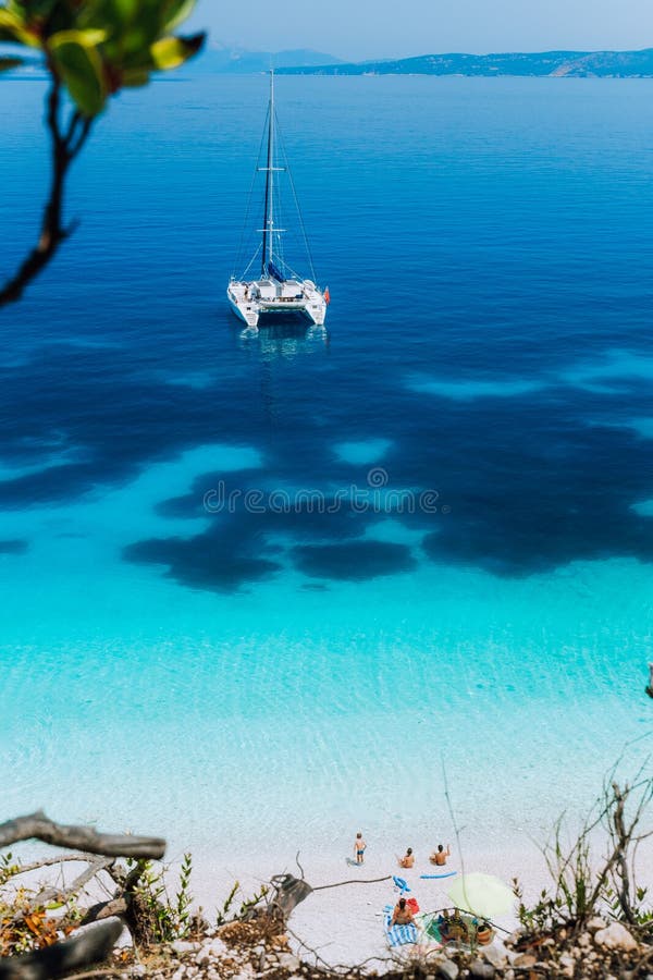 White catamaran yacht at anchor on clear azure surface with dark pattern in calm blue lagoon. Unrecognizable tourists stock photos White catamaran yacht at anchor on clear azure surface with dark pattern in calm blue lagoon. Unrecognizable tourists stock photos