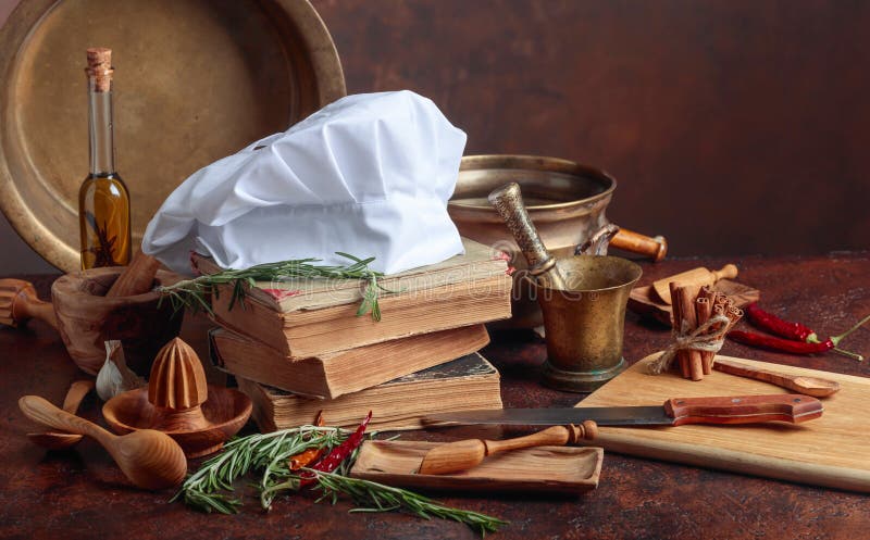 White chef`s hat and old cookbooks. Kitchen utensils with spices and rosemary on a kitchen table. Vintage rustic recipe book background stock images, royalty-free photos and pictures